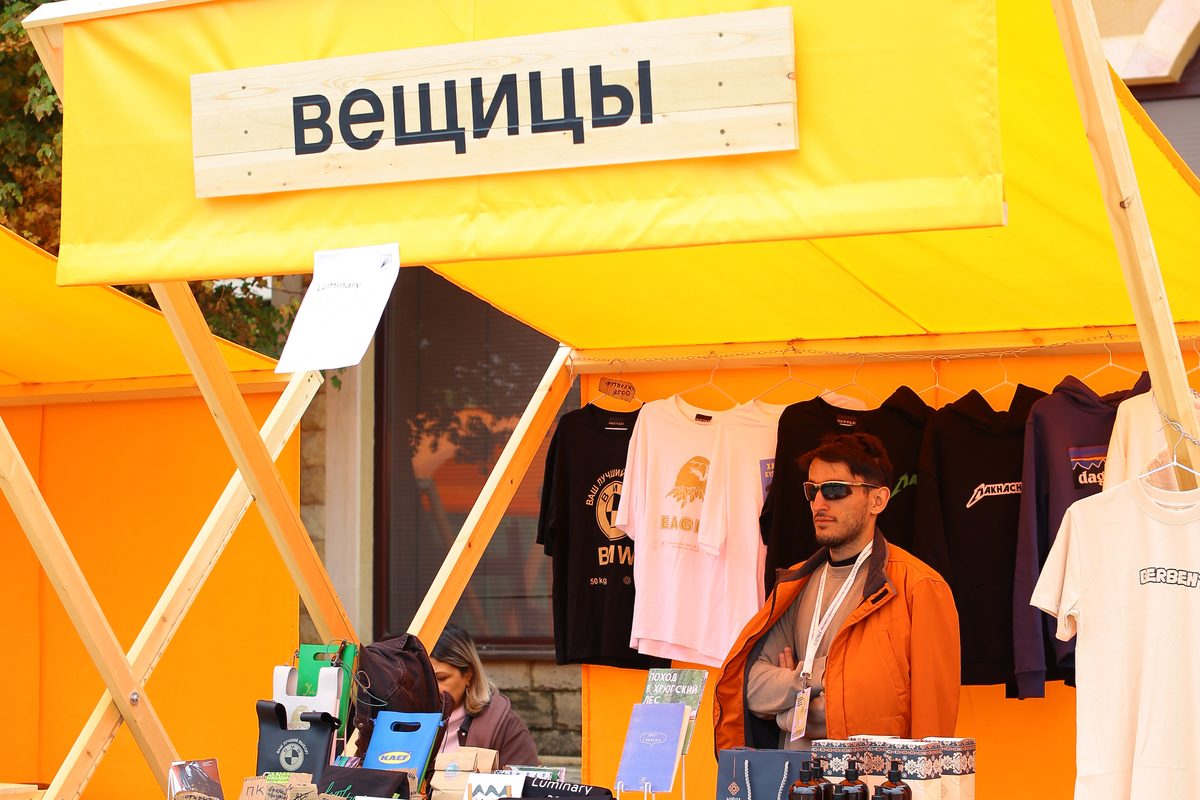 Павильон ярмарки с вывеской «вещицы»: футболки на вешалках и прилавок с изделиями местных марок
