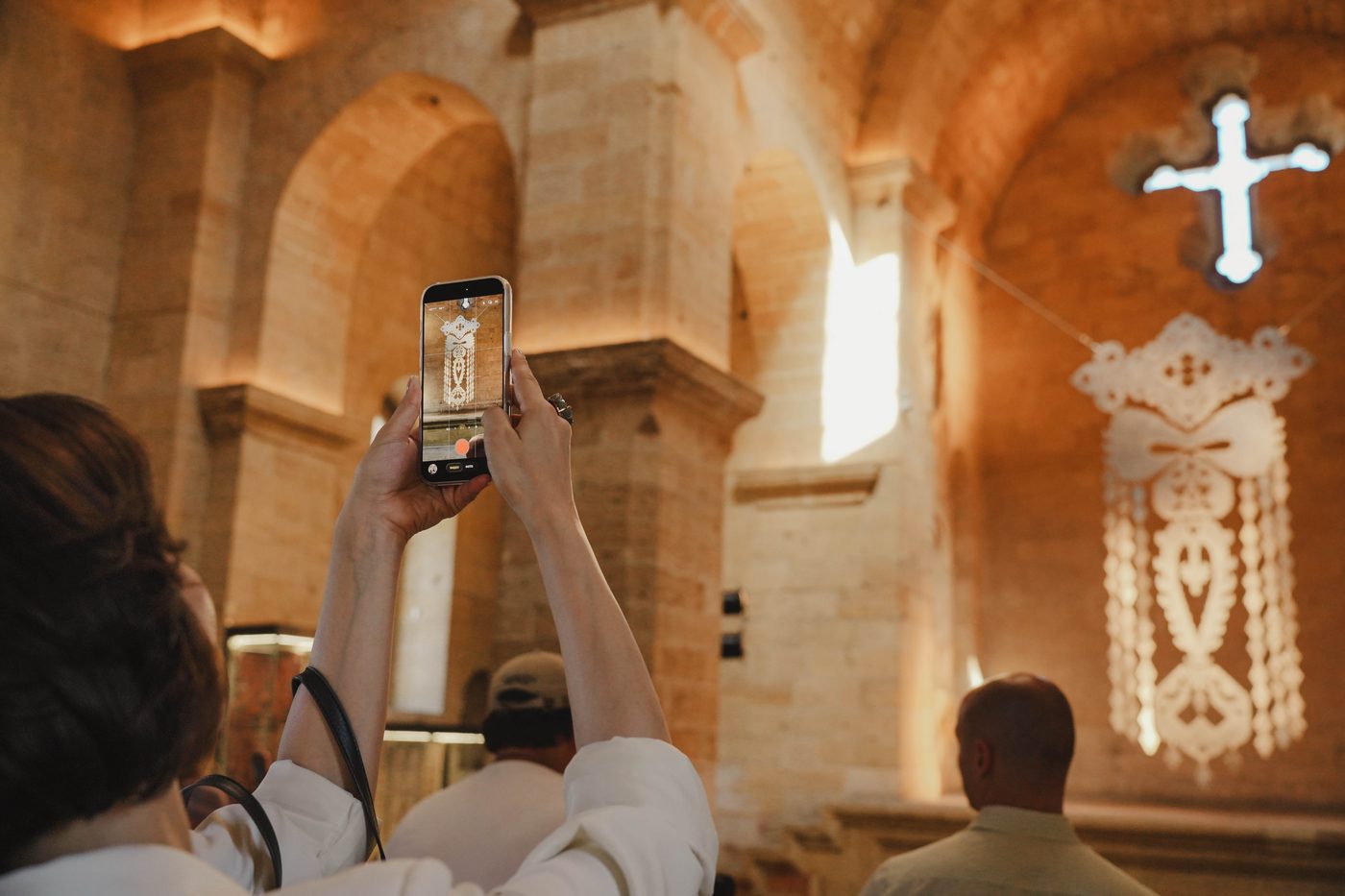 Посетительница снимает объект на телефон, за ней арки, белый крест и подвеска